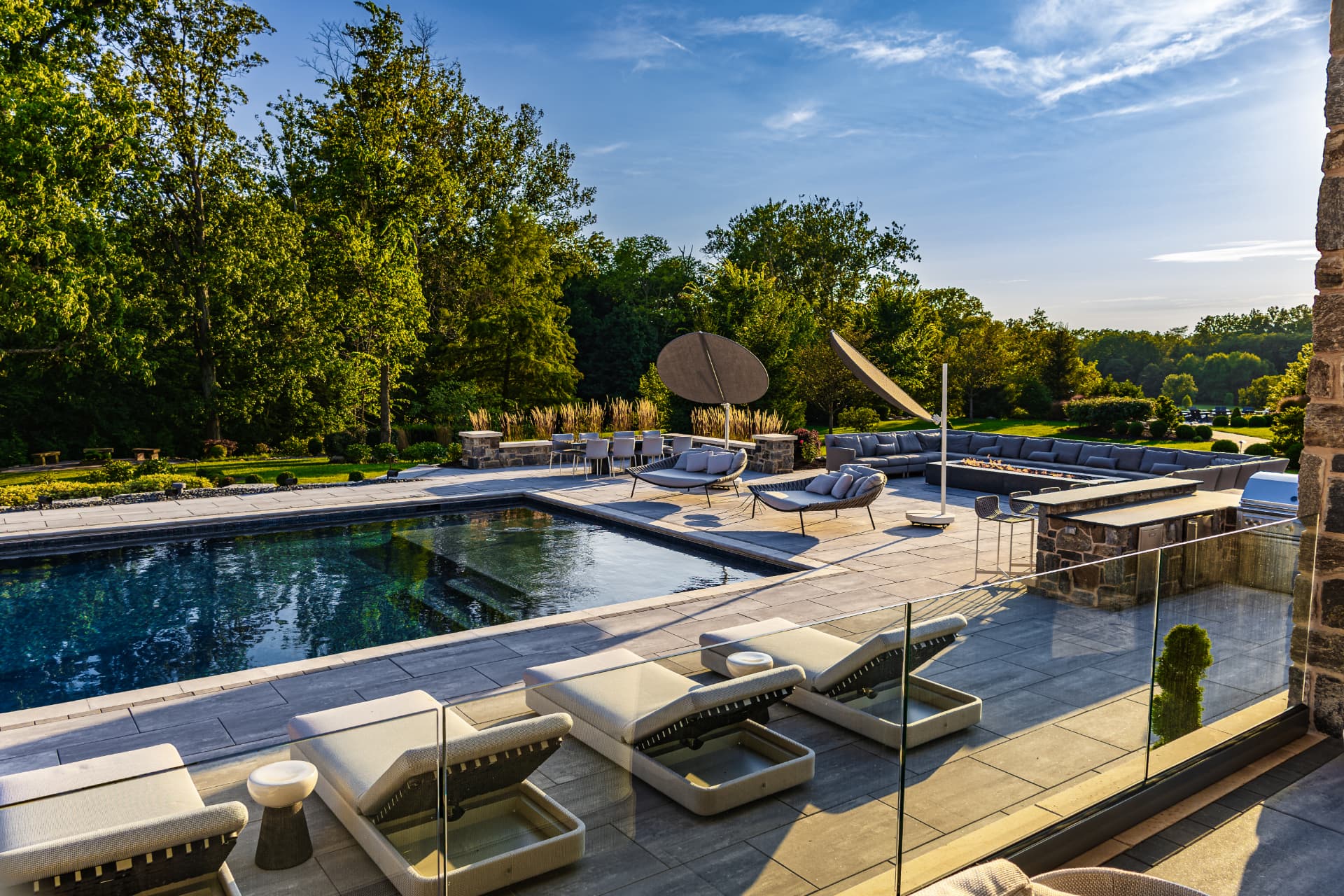 Luxury outdoor living space with a swimming pool, stone terrace, lounge seating, fire feature and mature landscape plantings
